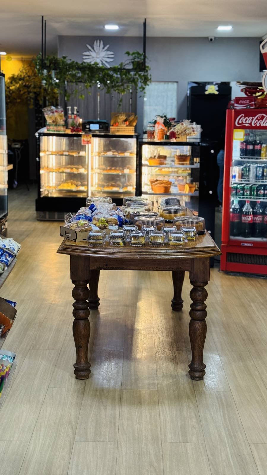 Vitrine de pães e doces da padaria Tia Ju, com geladeira de bebidas e mesa de bolos embalados